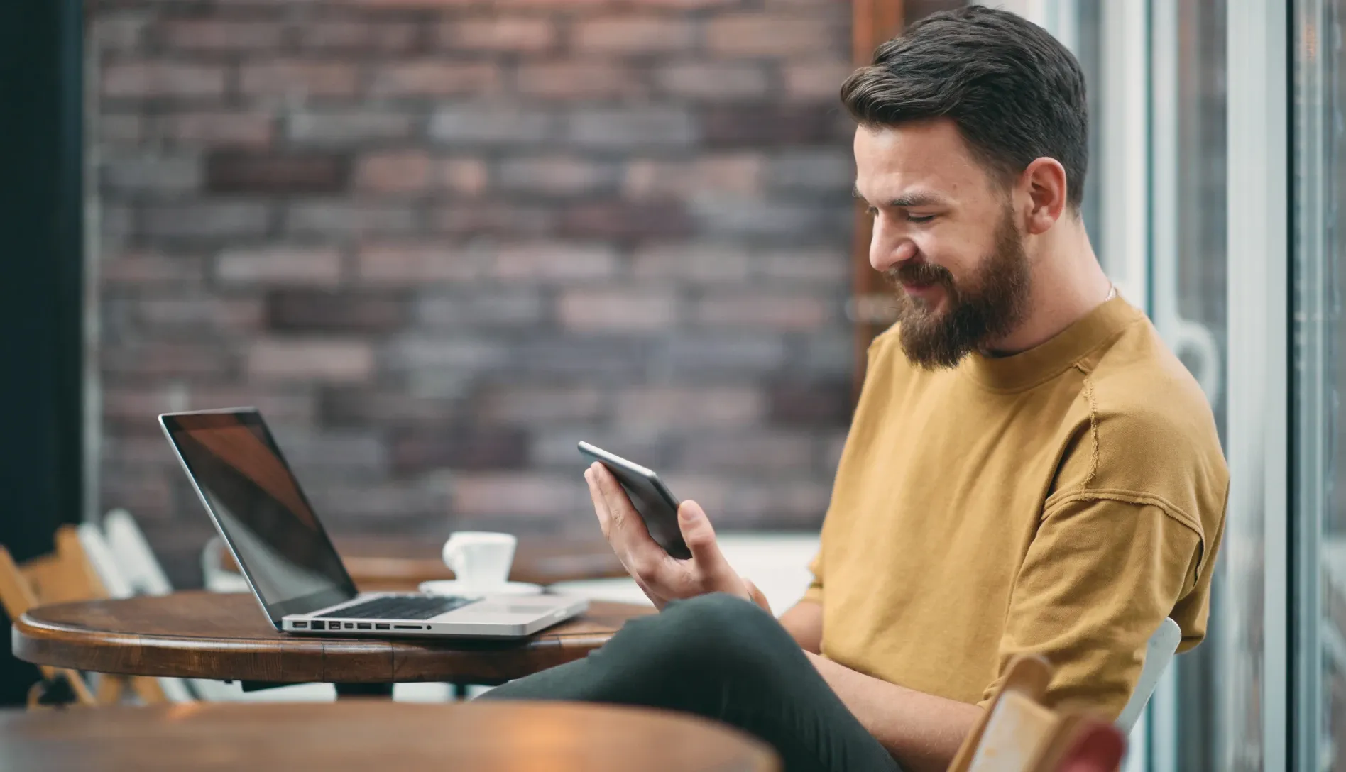 Homem com uma xícara de café, sorrindo enquanto olha para o smartphone.